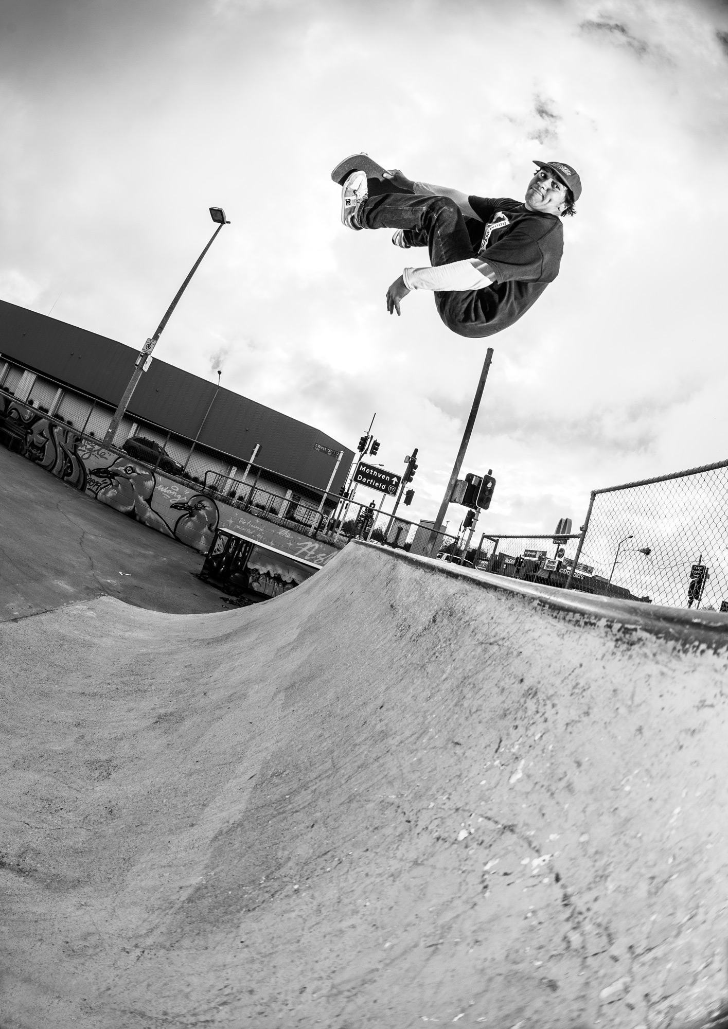 Black and white photo of Pauly Kauri doing a backflip at Ashburton Skatepark. The image is shot using a fisheye lens and is pointing up at Pauly from the ground.