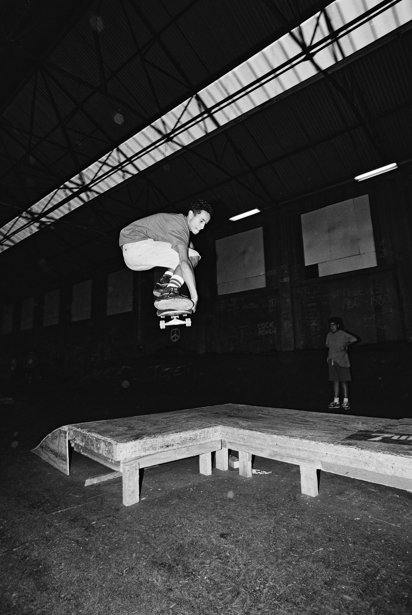 Chey Ataria performing an ollie mute grab off of a plywood wedge ramp obstacle at The Skate Pit in Wellington, 1990.